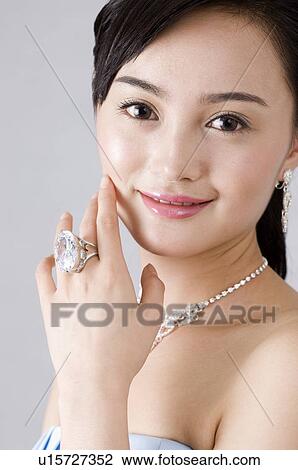 Stock Image - Smiling young woman with hand touching face, showing ring on finger, close-up. Fotosearch