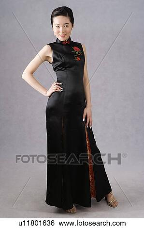 Stock Photograph - Young Chinese woman wearing a black cheongsam with embroidery, standing, smiling. Fotosearch