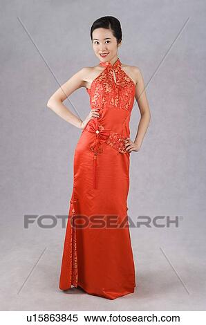 Stock Photography - Young Chinese woman wearing a red embroidered cheongsam, standing, arms akimbo. Fotosearch