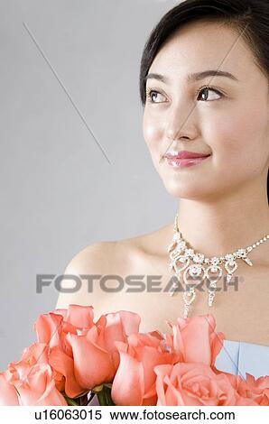 Stock Photography - Young woman dressed up, holding a bouquet of roses, looking up. Fotosearch