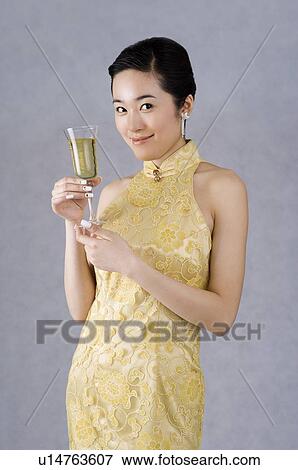 Stock Photo - Young woman in a yellow embroidered cheongsam, holding a glass of champagne. Fotosearch