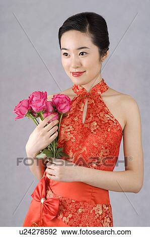Stock Image - Young woman in red cheongsam, holding pink roses. Fotosearch