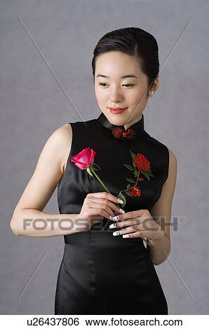 Stock Photograph - Young woman wearing a black cheongsam with floral embroidery, holding a pink rose. Fotosearch