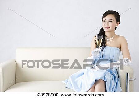 Young woman wearing a blue formal dress, sitting on sofa, holding a glass of champagne View Large Photo Image Stock Image - Young woman wearing a blue formal dress, sitting on sofa, holding a glass of champagne. Fotosearch