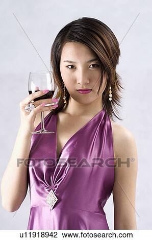 Stock Image - Young woman wearing a purple gown, dressed up, holding a glass of red wine. Fotosearch