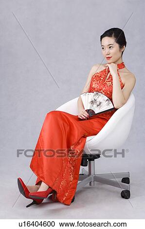 Young woman wearing a red embroidered cheongsam, holding a folding fan, sitting View Large Photo Image Stock Image - Young woman wearing a red embroidered cheongsam, holding a folding fan, sitting. Fotosearch