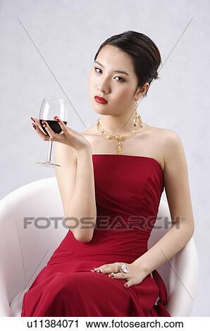 Young woman wearing a red evening dress and jewelry, holding a glass of red wine, head cocked View Large Photo Image Stock Image - Young woman wearing a red evening dress and jewelry, holding a glass of red wine, head cocked. Fotosearch