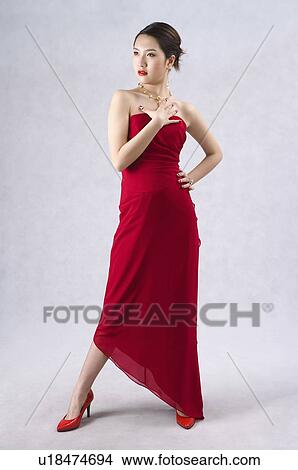 Picture - Young woman wearing a red evening gown and high heels, posing, head turned. Fotosearch