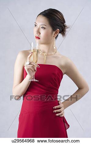 Stock Photo - Young woman wearing a red evening gown, holding a glass of champagne, hand on hip. Fotosearch