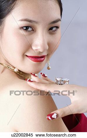 Stock Photography - Young woman with hand on shoulder, showing ring and artificial fingernails. Fotosearch