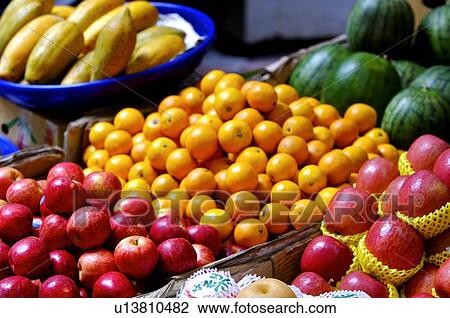 Stock Image - A variety of fruits including apples, oranges, papaya, and watermelons, on display at a market stall. Fotosearch