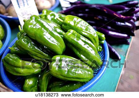 Stock Image - Green peppers on a plastic tray, next to a pile of dark purple eggplants. Fotosearch