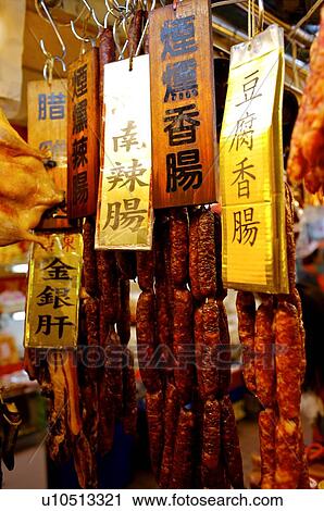 Stock Image - Preserved meat sausages with signs, hanging from hooks, on display in a market stall. Fotosearch