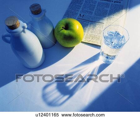 Stock Photography - Glass that is Reflecting Sunlight and Bottle and Newspaper and Apple, High Angle View. Fotosearch