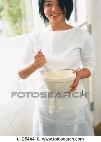 Stock Photo -  a Mid Adult Woman Cooking, Smiling, Wearing a White Apron, Front View. Fotosearch