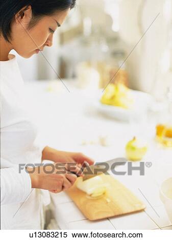 Stock Photography -  a Mid Adult Woman Cutting Some Vegetables in the Kitchen, Side View, Differential Focus. Fotosearch