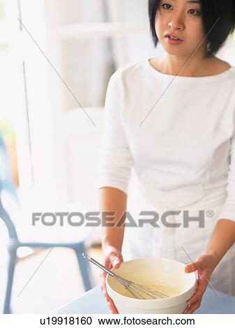 Stock Image -  a Mid Adult Woman Holding a White Bowl in her Hands, Looking Sideways, Front View, Differential Focus. Fotosearch