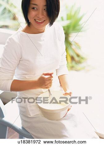 Stock Image -  a Mid Adult Woman Mixing Something in a White Bowl, Smiling, High Angle View. Fotosearch