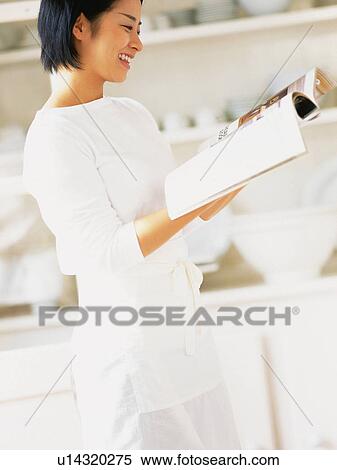 a Mid Adult Woman Reading a Magazine in the Kitchen, Smiling, Side View, Differential Focus View Large Photo Image Stock Photography - a Mid Adult Woman Reading a Magazine in the Kitchen, Smiling, Side View, Differential Focus. Fotosearch
