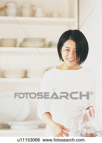 Stock Photograph -  a Mid Adult Woman Standing In Front of a White Cupboard Full of Dishes, Smiling, Looking at Camera, Front View, Differential Focus. Fotosearch