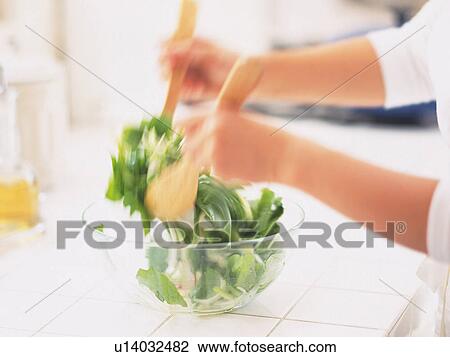 Stock Image -  a Person Mixing a Green Salad With Wooden Spoons, Side View, Blurred Motion. Fotosearch