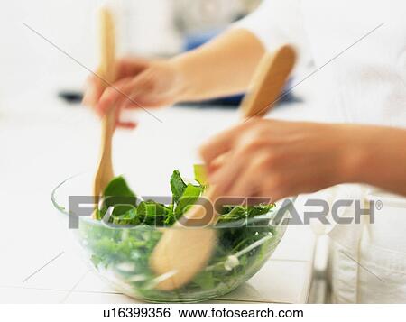 Stock Photograph -  a Person Mixing a Green Salad With Some Wooden Spoons, Side View, Blurred Motion. Fotosearch