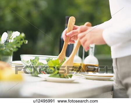 Stock Image -  a Person Putting Some Green Salad on a Plate Outdoors, Side View, Differential Focus. Fotosearch