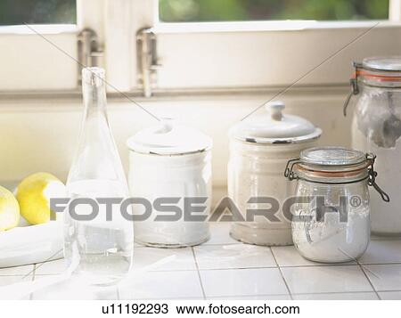 Stock Image -  Several Kitchen Items, Such as Bottles and Tins Next to a Window, Front View. Fotosearch