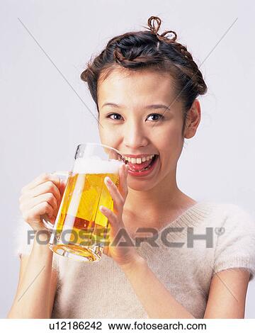 Stock Image - A Woman Drinking a Glass of Beer, Smiling, Looking at Camera, Front View. Fotosearch