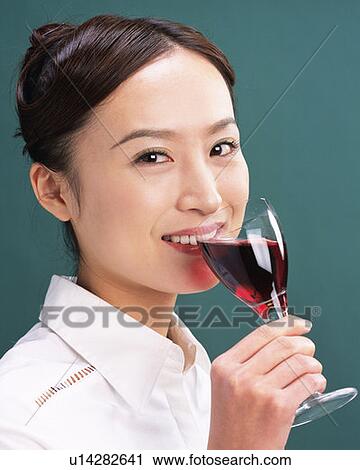 Stock Image - A Woman Drinking a Glass of Red Wine, Smiling, Looking at Camera, Side View. Fotosearch