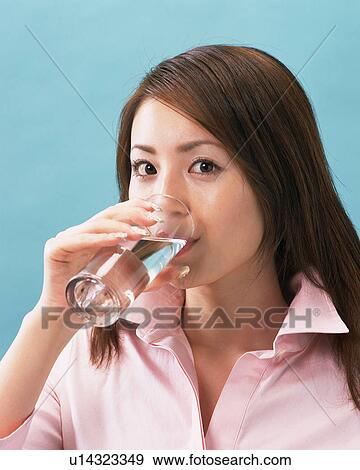 Stock Photo - A Woman Drinking Water, Looking at Camera, Side View . Fotosearch