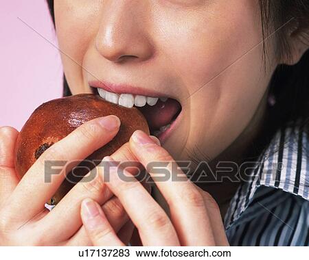 Stock Image - A Woman Eating a Bun, Front View, Close Up. Fotosearch