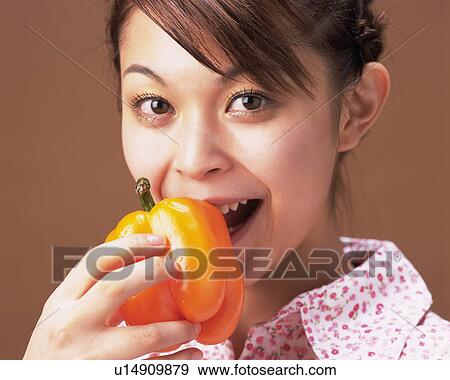 Stock Photo - A Woman Eating a Pepper, Looking at Camera, Front View. Fotosearch