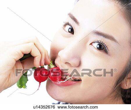 Stock Photograph - A Woman Eating a Radish, Looking at Camera, Side View. Fotosearch