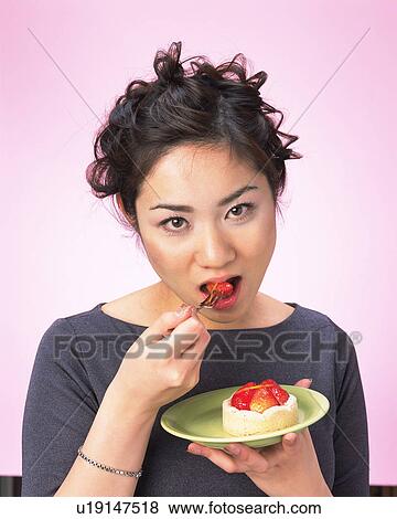 Stock Photo - A Woman Eating Cake, Looking at Camera, High Angle View. Fotosearch