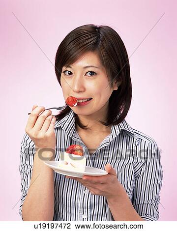 Stock Image - A Woman Eating Cake, Smiling, Looking at Camera, Front View . Fotosearch