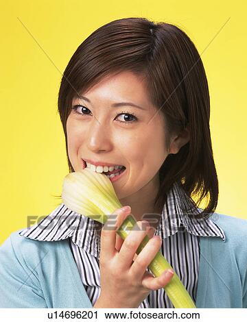 Stock Image - A Woman Eating Celery, Smiling, Looking at Camera, Front View. Fotosearch