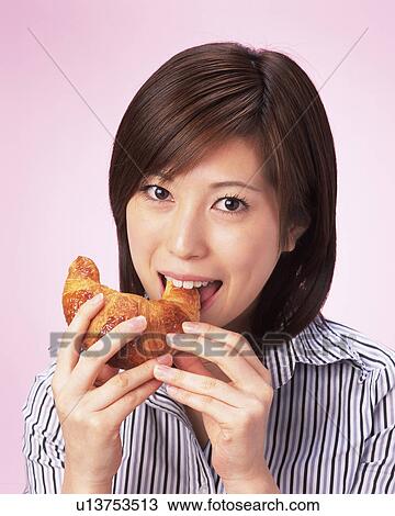 Stock Image - A Woman Eating Croissant, Looking at Camera, Front View . Fotosearch
