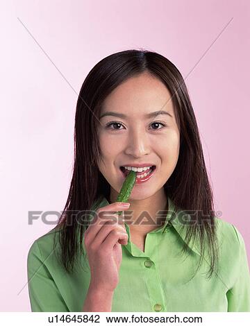 Stock Image - A Woman Eating Cucumber, Smiling, Looking at Camera, Front View . Fotosearch