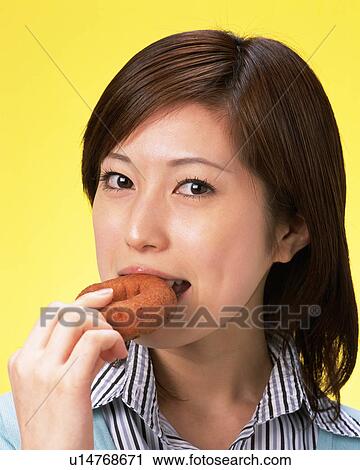 Stock Image - A Woman Eating Doughnut, Smiling, Looking at Camera, Front View . Fotosearch