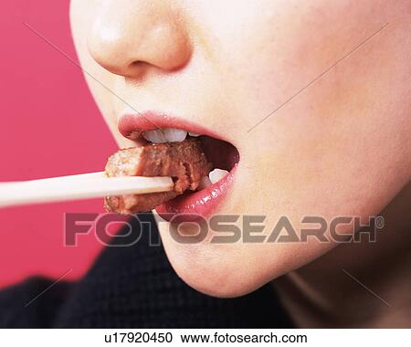 Stock Image - A Woman Eating Meat, Side View, Close Up. Fotosearch