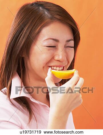 Stock Photo - A Woman Eating Orange, Smiling, Looking at Camera, Side View, . Fotosearch
