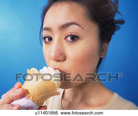 Stock Photograph - A Woman Eating Soft Ice-cream, Looking at Camera, Side View. Fotosearch