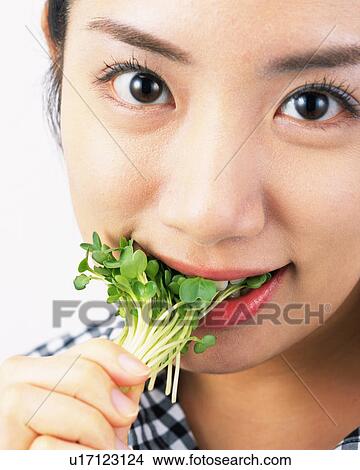 Picture - A Woman Eating White Radish Sprouts, Looking at Camera, Front View . Fotosearch