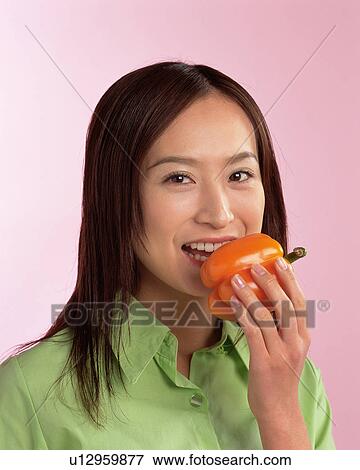 Stock Photo - A Woman Eating Yellow Pepper, Smiling, Looking at Camera, Front View . Fotosearch