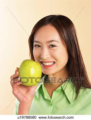 Stock Image - A Woman Holding Green Apple, Looking at Camera, Front View . Fotosearch