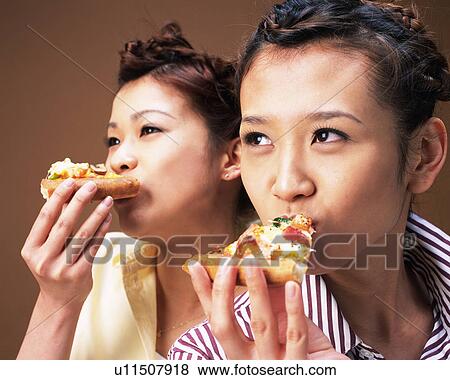 Stock Photo - Two Young Women Eating Pizza, Side View,. Fotosearch
