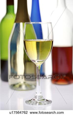 Stock Image - Filled wine glass in front of several wine bottles. Fotosearch