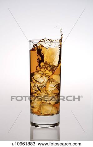 Stock Image - Glass of iced black tea, ice cube dropping into the glass and splashing drink out of the glass. Fotosearch