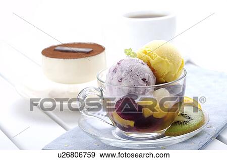 Stock Photo - Ice cream with fruit in a tea cup, and tiramisu and a coffee cup in the background. Fotosearch
